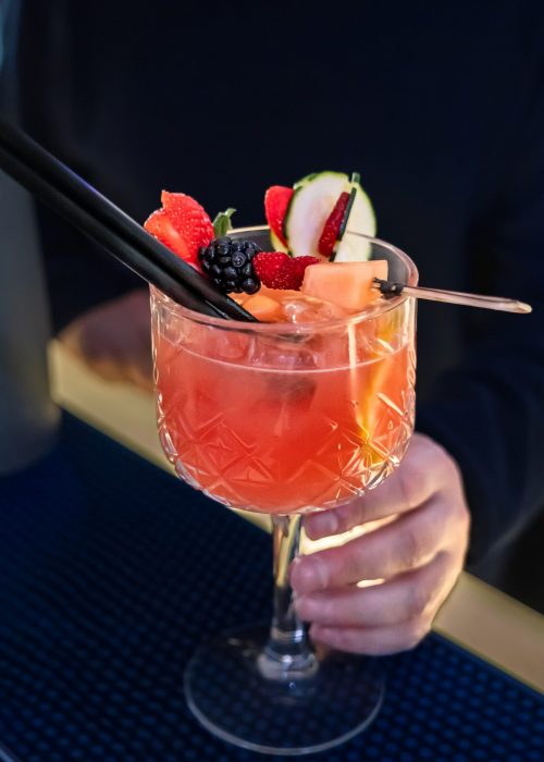 Unrecognizable bartender dressed in black serving a bitter orange cocktail with fruit garnish